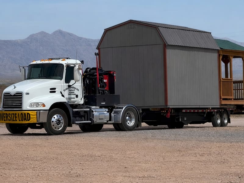 An oversize load truck hauling a portable building with mountains in the background