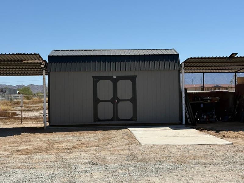 A gray lofted shed with double doors set between two carports