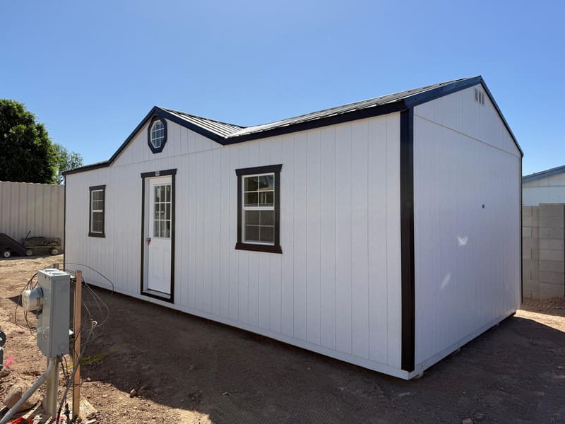 A white shed with black trim placed in a residential yard