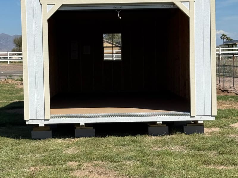 A cream-colored barn-style shed with its garage door open in a grassy yard