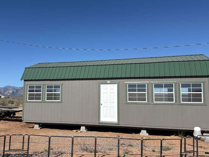 A green-roofed shed freshly delivered next to the hauling trailer, mountains in the background