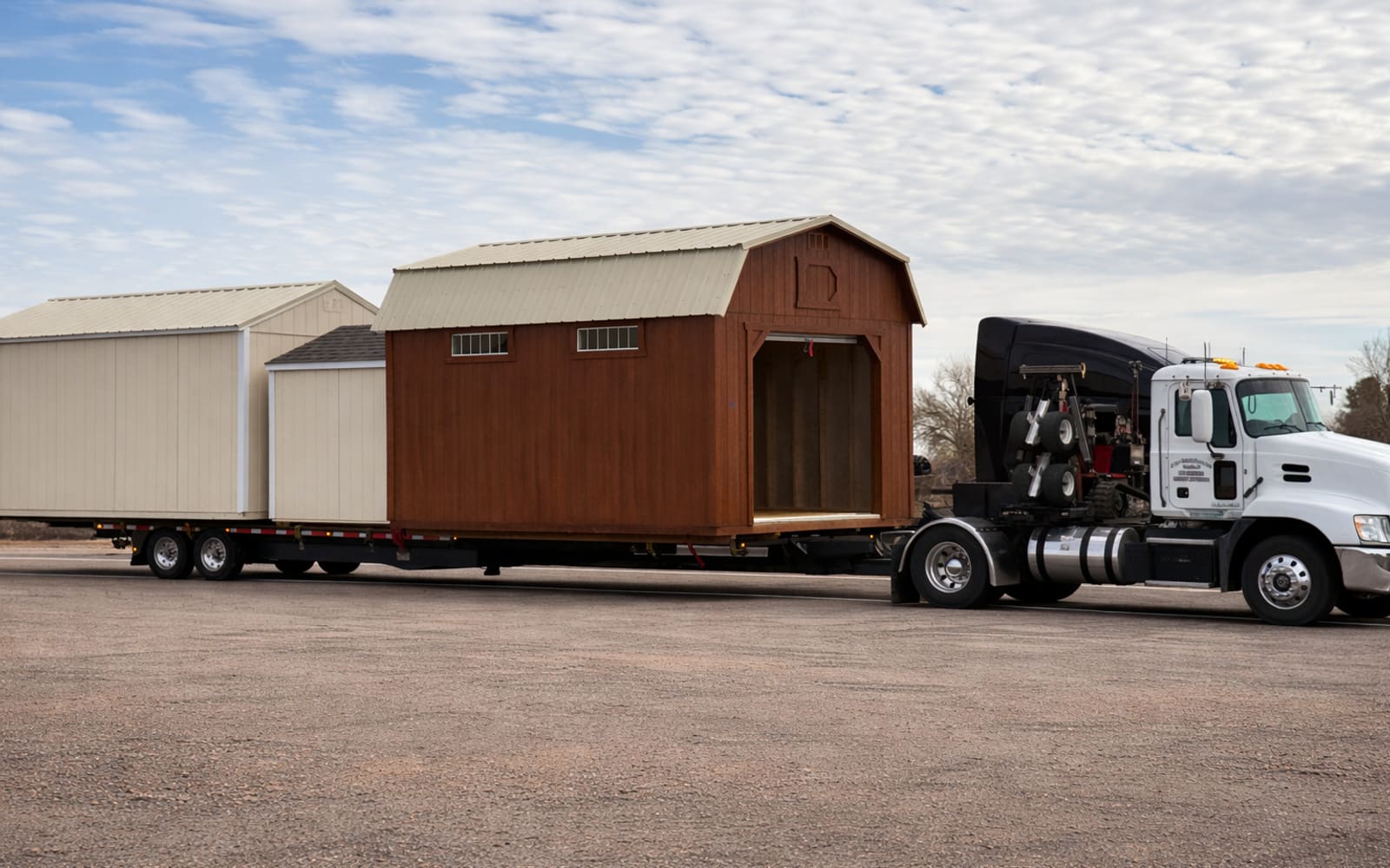 An S Bar Enterprises truck hauling several portable buildings on a flatbed trailer