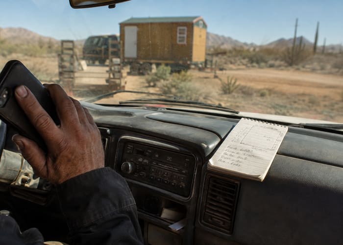 Reviewing a quote request from the truck, notes on a pad next to a portable building on site